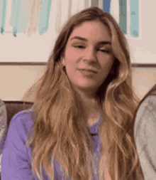 a woman with long blonde hair is wearing a purple shirt and making a face .