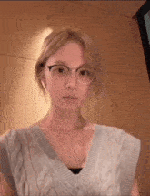 a woman wearing glasses and a sweater is looking at the camera .