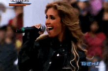 a woman singing into a microphone in front of a telehit sign