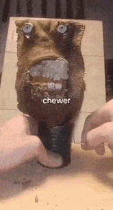 a person is holding a sculpture of a face with a mouth open and the word chewer above it .