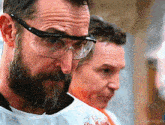 a man with a beard wearing safety goggles looks at the camera