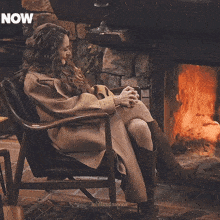 a woman is sitting in a chair in front of a fireplace and the word now is on the bottom