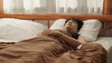 a man is sleeping on a bed with a brown blanket