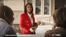 a woman in a red jacket is holding a bottle of wine in front of a nbc sign