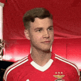a young man wearing a red and white soccer jersey is looking at the camera .