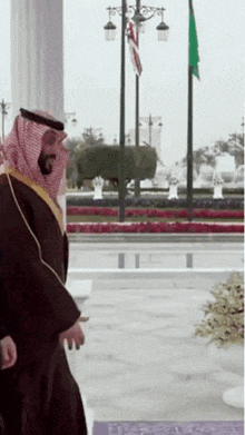 a man in a traditional arabic costume stands in front of a flag pole