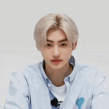 a young man with blonde hair is wearing a light blue shirt with a heart on it .