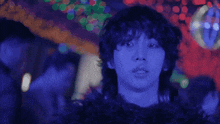 a man with blue hair stands in front of a disco ball in a dark room