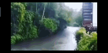 a truck is driving down a road next to a river in the woods .