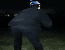 a person wearing a black jacket and a blue hat is standing in the dark