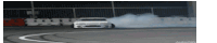 a white car is drifting on a track with smoke coming out of the tires .