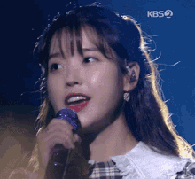 a close up of a woman singing into a microphone with kbs written on the bottom