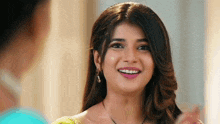 a woman is smiling and looking at the camera while wearing earrings and a necklace .