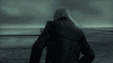 a man in a black jacket is standing in front of a body of water in the dark .