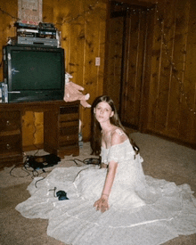 a woman in a white dress is sitting on the floor in front of a tv