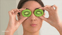 a woman is holding slices of kiwi over her eyes