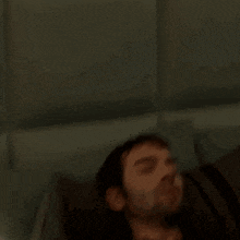 a man with a beard is sleeping in a bed with his eyes closed