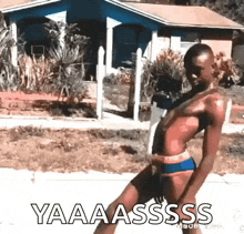 a man in a bikini is walking down the street with the words yaaaassss written on the sidewalk .