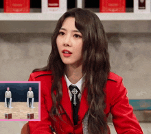 a woman in a red jacket and tie is sitting in front of a picture of two people dancing