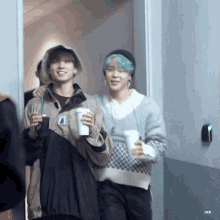 a couple of men are standing next to each other holding cups of coffee .
