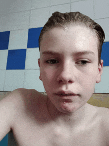 a young boy without a shirt is taking a selfie in front of a blue and white tiled wall