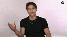 a young man wearing a black t-shirt and a chain around his neck talks to someone
