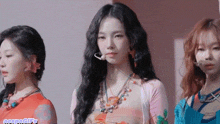 three women are standing next to each other in a room and one of them is wearing a necklace .
