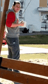 a man in a red shirt and grey sweatpants is standing next to a wooden fence