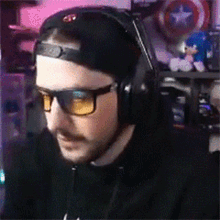 a man wearing headphones and sunglasses is sitting in front of a computer monitor .