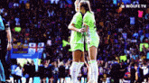 two female soccer players hugging each other in front of a crowd with a wolfe tv logo on the bottom right