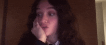 a woman with curly hair is sitting in front of a wooden door with her hand on her face .