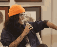 a woman wearing an orange hat and glasses is holding a microphone and smiling