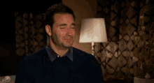 a man covering his face with his hands in a room with a lamp