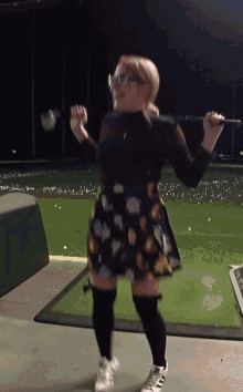 a woman in a floral skirt is holding a golf club in her hands