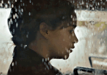 a close up of a woman 's face behind a window with water drops on it