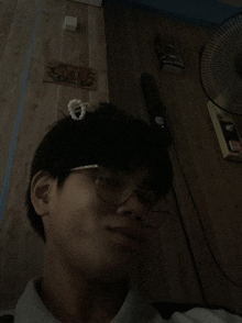 a man wearing glasses has a flower on his head and a box of cigarettes on the wall behind him