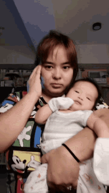 a woman wearing a mickey mouse shirt holds a baby
