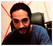 a man with a beard is sitting in a chair and making a funny face .