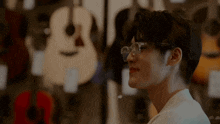 a young man wearing glasses is standing in front of a wall of guitars
