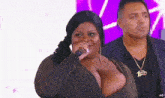 a woman in a very revealing dress is singing into a microphone while a man looks on .