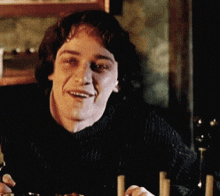 a man in a black sweater is smiling and holding a glass of wine