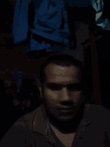 a man with a beard and a blue shirt is laying down in a dark room