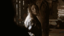 a woman is standing in a dark room with a horse in the background