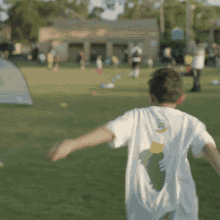 a boy wearing a white shirt with a green and yellow design on the back is running in a field