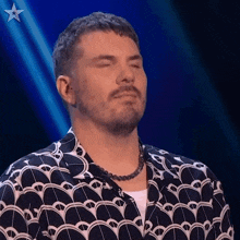 a man with his eyes closed is wearing a necklace and a shirt with a pattern .