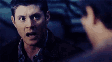 a man with his mouth open is talking to another man in a dark room .