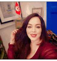a woman in a red shirt is smiling in front of a flag