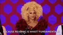 a drag queen with a big blonde afro is wearing a red dress and says `` because reading is what ? fundamental !! ''
