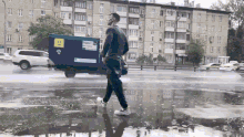 a man walking in the rain with a blue truck behind him that has a yellow sticker that says ' a ' on it