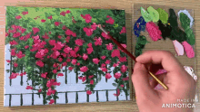 a painting of pink flowers is being painted on a canvas by a person